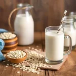 Oat milk in a glass with oats and a plant sprig on a wooden table.