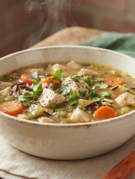 Hearty slow cooker chicken and wild rice soup in rustic bowl with fresh parsley garnish