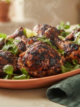 Oven-baked Jamaican jerk chicken with caramelized skin on terracotta platter with lime and cilantro